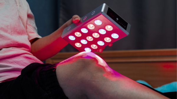 a man holding a small red light panel towards his knee